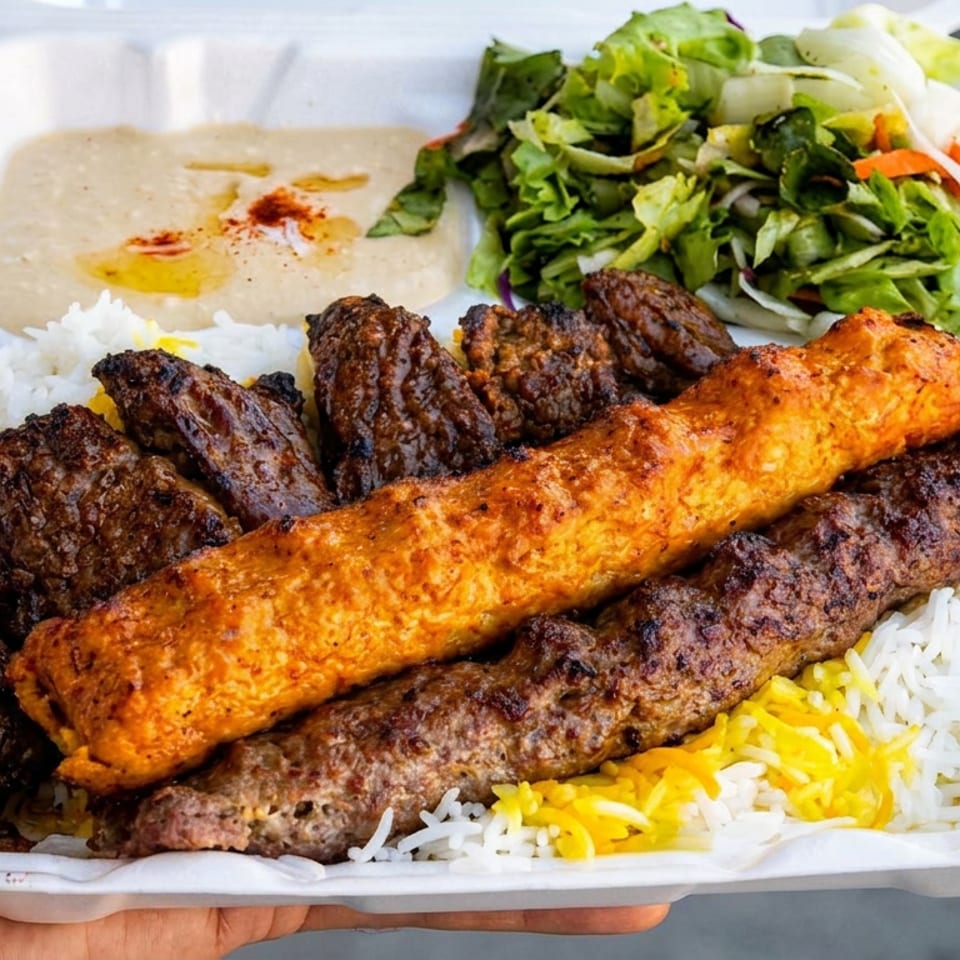 Takeout platter with grilled kebabs, orange chicken skewer, basmati rice, hummus, and green salad in a foam container.